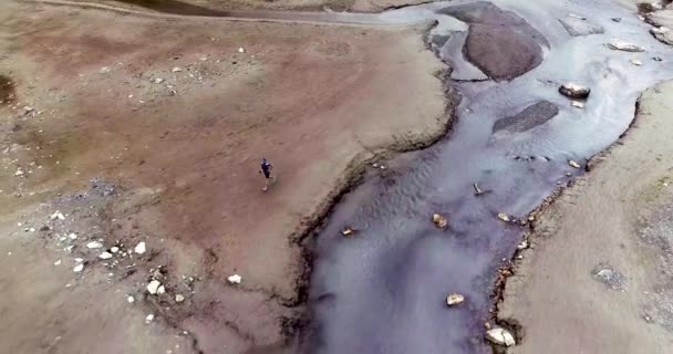 Letecký pohled na muže běžícího v pestrobarevné rovině poblíž temné řeky. Červený písek, bílé kameny a štěrk na podlaze — Stock video