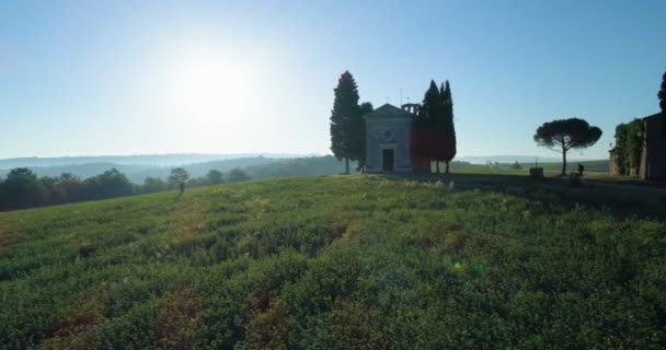 Toskana 'daki renkli kırların havadan görünüşü. Güneş ufukta batıyor. Mavi gökyüzü, yeşil tepe, tarım arazisi ve terk edilmiş bir kilise.. — Stok video