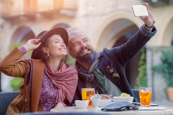 Feliz pareja amorosa disfrutando en la cafetería bar al aire libre, restaurante.Love, citas, comida, estilo de vida.Novio y novia sentado en un bar, beber aperitivo spritz, tomar fotos en un centro histórico Imagen De Stock