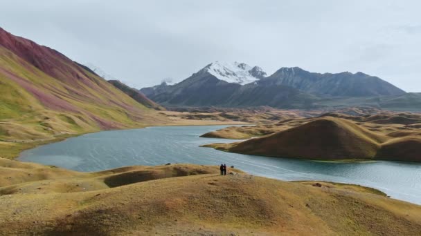 Foto aérea de un hermoso valle con montañas circundantes, dos personas en la cima de la colina. El río cruzó el valle verde y marrón durante el día soleado.Tayikistán — Vídeos de Stock