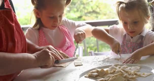 Primer plano de dos chicas cocinando pasta con la abuela. Momento divertido de dos niños aprendiendo a hacer pasta con la abuela. — Vídeos de Stock