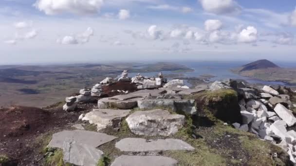 Panoramic Walking along stone path in irish mountain in a sunny day with clouds in summer.village down the valley,sea and mountain range in the background. Dry and arid meadow,grass,rocks. — Stock Video