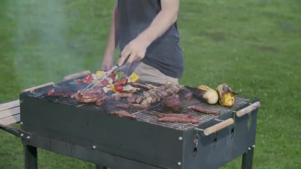 Homem irreconhecível cozinhando kebabs em uma churrasqueira no verão.Close-up de homem cozinhando alimentos na churrasqueira whilst.steaks e espetos na churrasqueira quintal — Vídeo de Stock