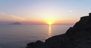 Deniz üzerindeki renkli günbatımının havadan görünüşü, Aeolian adaları. Su yüzeyine yansıyan güneş. Mor, kırmızı, mavi, turuncu alacakaranlık. Yaz günbatımında adaların silueti. Yavaş çekim
