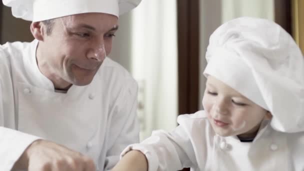 Papá e hijo jugando con harina mientras cocinan pastel. Actividades familiares, hijo aprender a hacer pastel de papá. Momentos divertidos, felicidad — Vídeo de stock