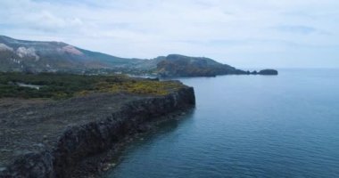 Sicilya 'da bulutlu bir günde kayalık kıyı manzarası. Mavi deniz, arka planda dağlar. Güzel Akdeniz suları kayalık kıyılarla buluşur. Gezginler için vahşi doğa. 