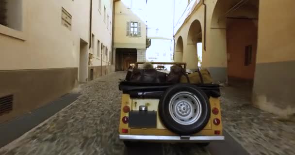 Visão traseira aérea do homem dirigindo carro amarelo com sua namorada ao lado dele em uma cidade característica e desolada na Itália — Vídeo de Stock