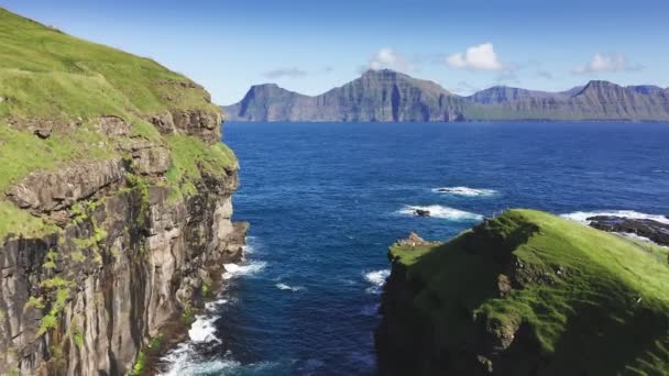 Drone che vola sopra erba coperto scogliera e mare. Gabbiani che sorvolano blu mare agitato vicino drone. Sullo sfondo montagna e scogliera in una giornata di sole estivo. — Video Stock