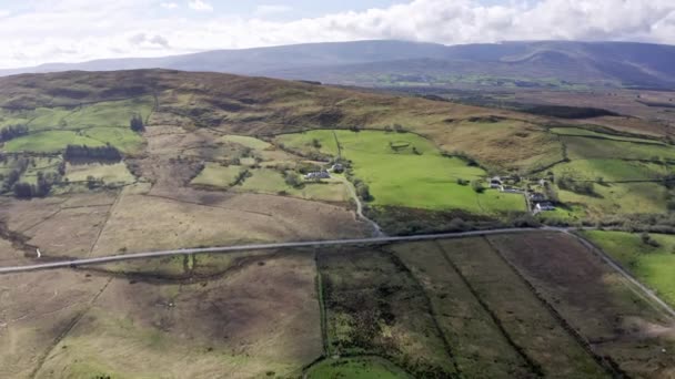 Flygfoto över grön jordbruksmark i Irland. irländskt landsbygdslandskap, panorama, liten by, tom väg, kullar i bakgrunden — Stockvideo