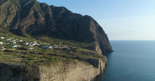 Costa rocosa panorámica y pintoresca durante la puesta del sol con campos verdes, árboles y pequeño pueblo. Vista aérea de la costa de Sicilia en un viaje de verano. — Vídeos de Stock