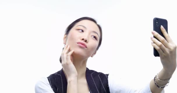 개인 행동 . Medium shot, A beautiful asian carefree woman 의 초상화 스마트폰으로 셀피를 복용. 웃는 얼굴을 하는 여자. 하얀 배경 위에 포즈를 취하는 긍정적 인 여성은 거짓말을 하지 않습니다. 4k 비디오 — 비디오