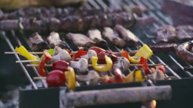Peppers, Green Chilies, Corn, Onion, Hamburgers, Brats, and Kabobs arranged on a bbq grill. Close up of young caucasian man cooking meat for the bbq.