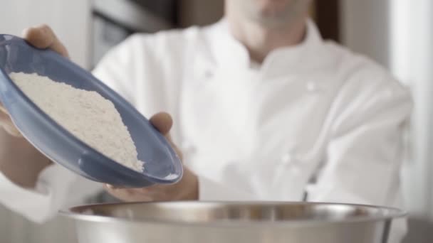 Il primo piano di mani di uomo spruzza la farina in una boccia per fare una torta. pasticcere porta un piatto con farina e versarlo in una ciotola d'acciaio. — Video Stock