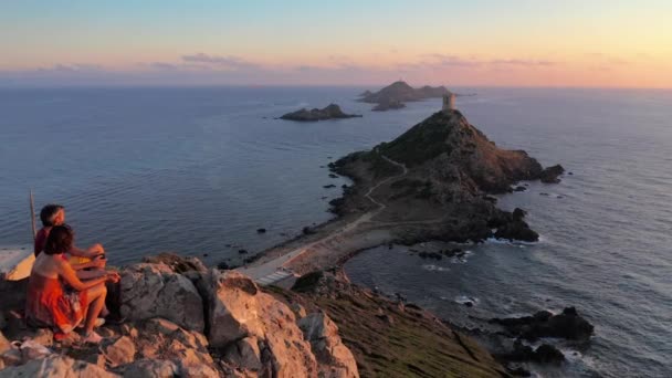 Vista aérea de dos personas mirando la puesta de sol del mar en la colina rocosa de la montaña. Drone shot of sea during colorful sunset, rocky island,couple watching the ocean at the edge on top of a rocky seashore in sundown — Vídeos de Stock