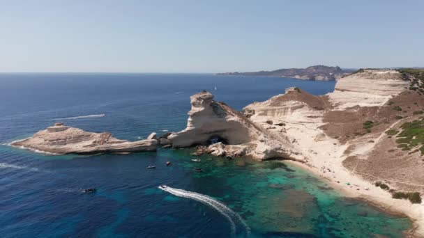 Kıyı şeridinde, mavi denizde dalgalarla birlikte Beyaz Bluff plajının yörüngesel hava manzarası. Bonifacio Korsika yakınlarında teknesiyle turkuaz denizde uçsuz bucaksız bir uçurum görüntüsü. — Stok video