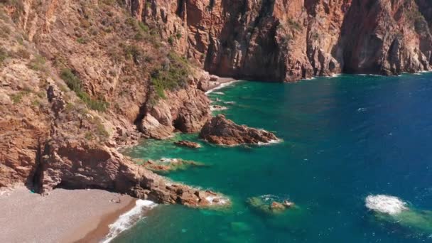 Veduta aerea di scogliere di roccia rossa montagna, spiaggia di sabbia, onde che si frantumano sulla spiaggia. Mare colorato, turchese blu, alte scogliere rosse su entrambi i lati, cespugli verdi di vegetazione. — Video Stock