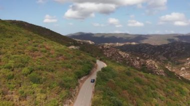 Güneşli yoldan dağ manzarasına giden elektrikli arabanın hava görüntüsü. Ağaçlar ve tarlalar boyunca hızla giden modern lüks bir araç yenilenebilir enerji ile.