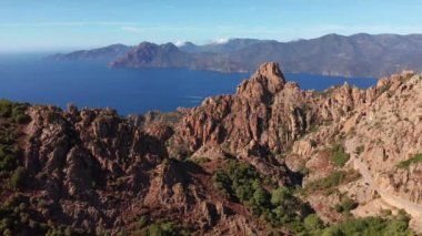 Kayalık kızıl dağın panoramik hava manzarası, güneşli bir yaz gününde arka planda deniz bulunan kanyon. Karakteristik kaya dağları, mavi deniz, mavi gökyüzü, güneşli gün. Korsika Kalkanları.