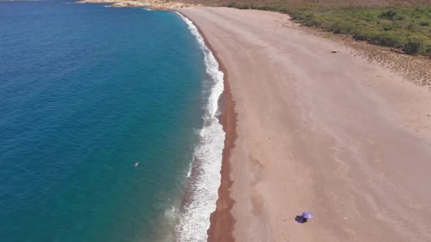 Luchtfoto van het verlaten rode zandstrand op een warme zomerdag. Golven crashen naar het strand, berg met struiken op de achtergrond, blauwe zee. Geen vervuiling en geen menselijk ingrijpen — Stockvideo