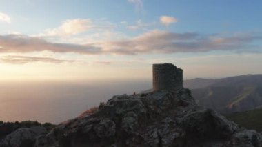 Günbatımında denize bakan eski ve eski binaların hava manzaralı güzel manzarası, etraftaki yeşil orman. Dağın tepesinde görünen iki kişi, altın deniz, bulutlar, dağ kıyıları.