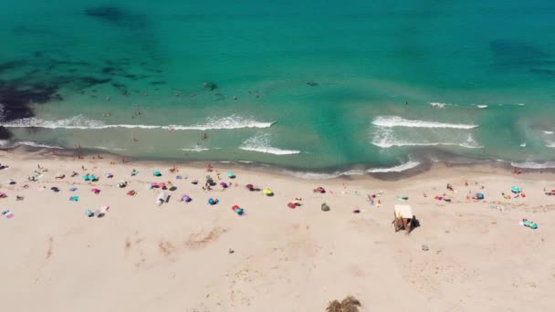 Flygfoto över vit sandstrand i en varm sommardag. Vågor kraschar till stranden, berg med buskar i bakgrunden, blått hav. Ingen förorening.Folk på stranden kopplar av, simmar, solar — Stockvideo