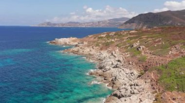 Beyaz kayaların havadan görünüşü, kurak bitki örtülü tepeler, kumsal, kumsala vuran dalgalar. Renkli deniz, mavi turkuaz, yeşil bitki çalıları..