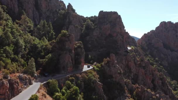 Panoramatický letecký výhled na skalnatou červenou horu, kaňon s elektrickým autem jedoucím v zakřivené silnici v letním slunném dni. Charakteristické skalní hory, modrá obloha, slunečný den.Korsika Calanques. — Stock video