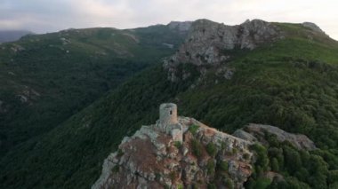 Dağın tepesindeki eski anıtın havadan görünüşü. Arka planda sıradağlar, yeşil orman, bulutlar, kayalar.