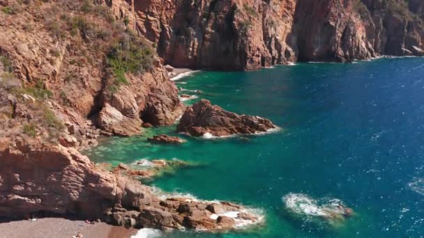 Vista aérea de penhascos de rocha vermelha montanha, praia de areia, ondas esmagando na praia. Mar colorido, azul turquesa, falésias vermelhas altas de ambos os lados, arbustos verdes de vegetação. — Vídeo de Stock