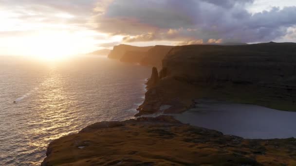 Vista aérea do lindo pôr-do-sol laranja na Ilha Faroé. Enorme penhasco e pilhas de mar brilham na luz dourada da noite — Vídeo de Stock