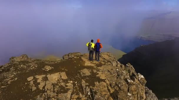 Letecký pohled na dva lidi na vrcholu hory s výhledem na krásnou krajinu, moře, útes, hora, skalnaté, obtékání mraky — Stock video