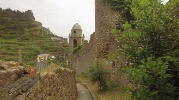 Promenade par ruelle caractéristique en Ligurie. Mur en pierre fait à la main du côté et de l'église. En arrière-plan montagne verte — Video