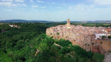 Hava manzaralı antik binalar, güneş ışığı, Pitigliano, Toskana. Ortaçağ mimarisi dağ tepesinde, çam ormanı boyunca kıvrımlı yol. Evlerde güneş parlıyor