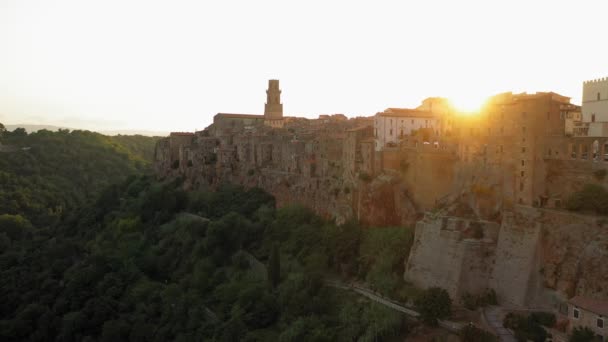 Letecký pohled na starobylé budovy při západu slunce, Pitigliano, Toskánsko. Středověká architektura horského kopce, křivolaká cesta borovým lesem. Slunce svítí skrz domy — Stock video