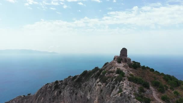 Aerial view of ancient and medieval building on the top of mountain,rocky coastline with green vegetation,down blue sea. In the background horizon line, clouds, island,in a summer day. — Stock Video