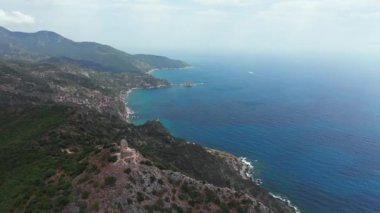 Dağın tepesindeki antik ve ortaçağ binasının havadan görünüşü, yeşil bitki örtülü kayalık kıyı şeridi, aşağı mavi deniz. Beyaz kayalar, ağaçlar. Dalgalar boş bir plaja çarpıyor, mavi gökyüzü bir yaz günü..