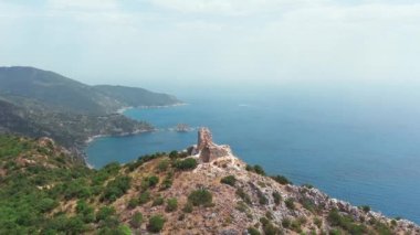 Dağın tepesindeki antik ve ortaçağ binasının havadan görünüşü, yeşil bitki örtülü kayalık kıyı şeridi, aşağı mavi deniz. Beyaz kayalar, ağaçlar. Dalgalar boş bir plaja çarpıyor, mavi gökyüzü bir yaz günü..