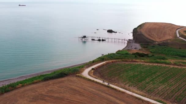 Aerial view of summer sunset,two people riding bike on a dirty road,bike hobby sport, outdoor activities.background wooden bridge construction in the sea, ocean,arid meadow and agricultural fields. — 비디오