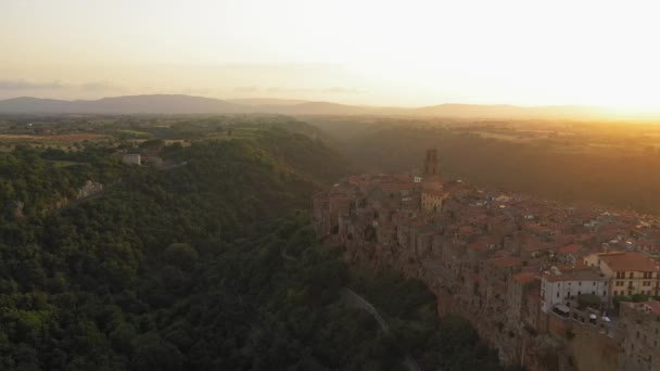 Pandangan udara bangunan kuno selama matahari terbenam, Pitigliano, tuscany. Arsitektur abad pertengahan o gunung bukit, melengkung jalan melalui hutan pinus. Matahari bersinar melalui rumah-rumah — Stok Video