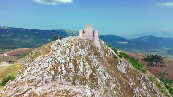 Aerial view of ancient castle on mountain hill, pine forest on mountain slope.White rocks and curved dirty road along the mountain. Mountain range in the background with blue sky un a summer sunny day — Stock Video