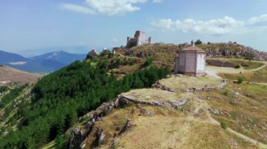 Dağ tepesindeki eski şatonun havadan görünüşü, dağ yamacındaki çam ormanı. Beyaz kayalar ve dağ boyunca kıvrımlı kirli yollar. Arka planda mavi gökyüzü olan dağ sıraları güneşli bir yaz günü