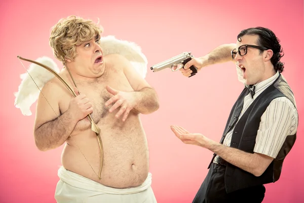 Hombre nerd con gafas amenaza a Cupido con pistola para robar arco de amor y flecha para el día de San Valentín — Foto de Stock