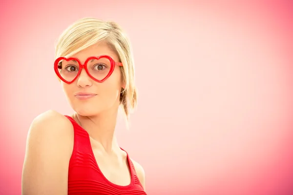 Joven hermosa mujer con gafas en forma de hogar en vestido rojo sonrisa en rosa para el día de San Valentín —  Fotos de Stock