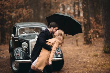 Şık Loving düğün çift öpüşme ve retro car yakınındaki bir çam ormanı içinde sarılma