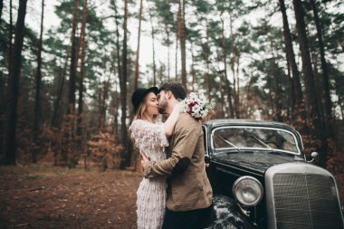 Şık Loving düğün çift öpüşme ve retro car yakınındaki bir çam ormanı içinde sarılma