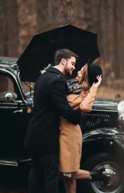 Şık Loving düğün çift öpüşme ve retro car yakınındaki bir çam ormanı içinde sarılma