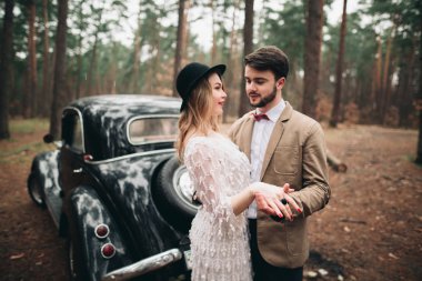 Şık Loving düğün çift öpüşme ve retro car yakınındaki bir çam ormanı içinde sarılma