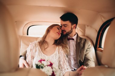 Gorgeous newlywed bride and groom posing in pine forest near retro car in their wedding day