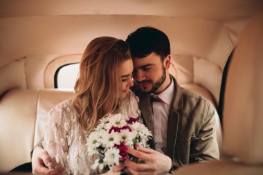 Gorgeous newlywed bride and groom posing in pine forest near retro car in their wedding day
