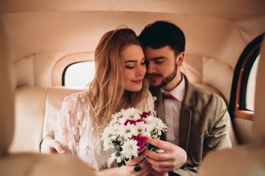 Gorgeous newlywed bride and groom posing in pine forest near retro car in their wedding day